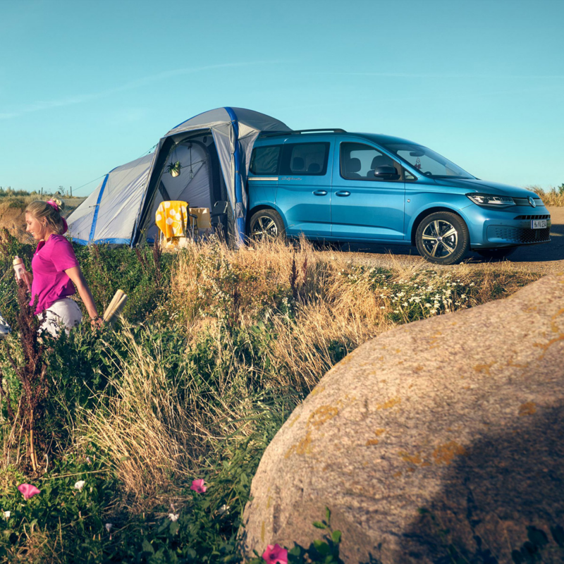 Una tienda de campaña desplegada junto al VW Caddy en un camino de campo.