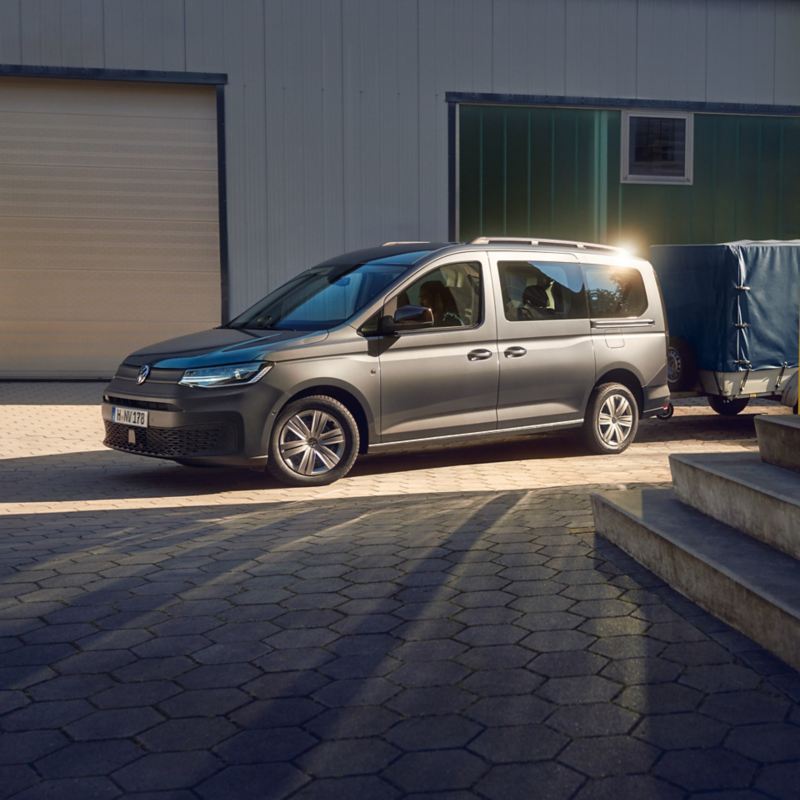 Ein Volkswagen Caddy Kombi mit Anhänger steht vor einem Häuserkomplex.