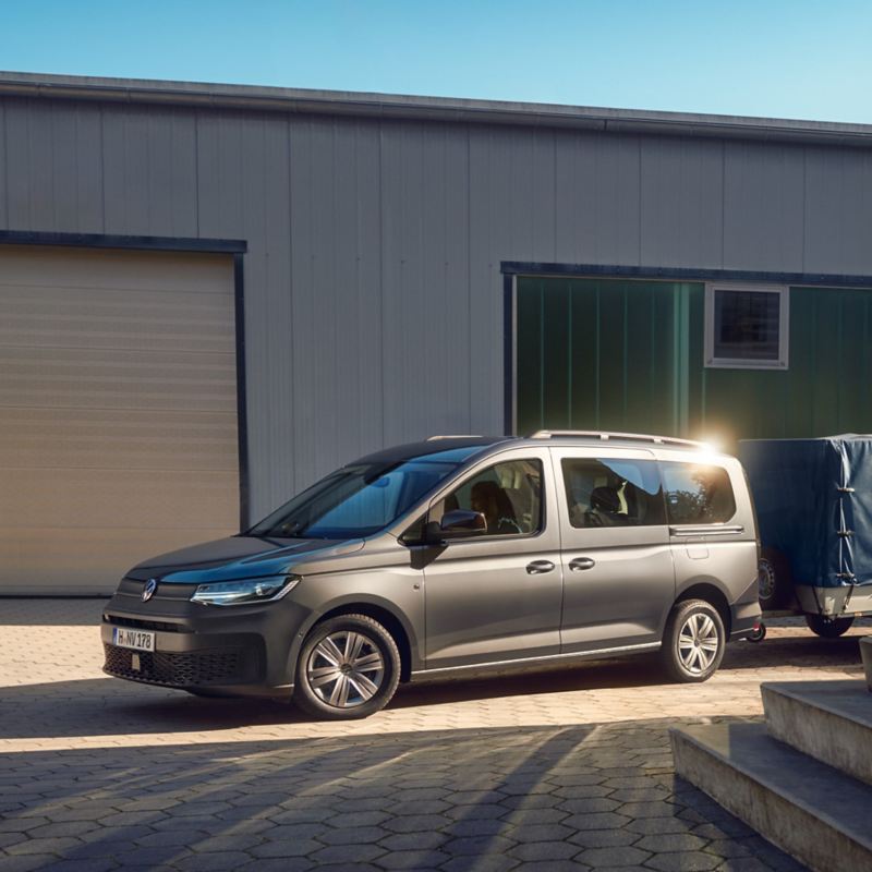 Ein Volkswagen Caddy Kombi mit Anhänger steht vor einem Häuserkomplex.