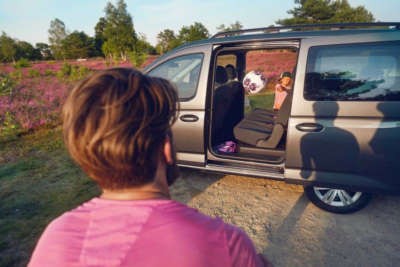 Dziecko rzucające piłką przez otwarte przesuwane drzwi VW Caddy Kombi.