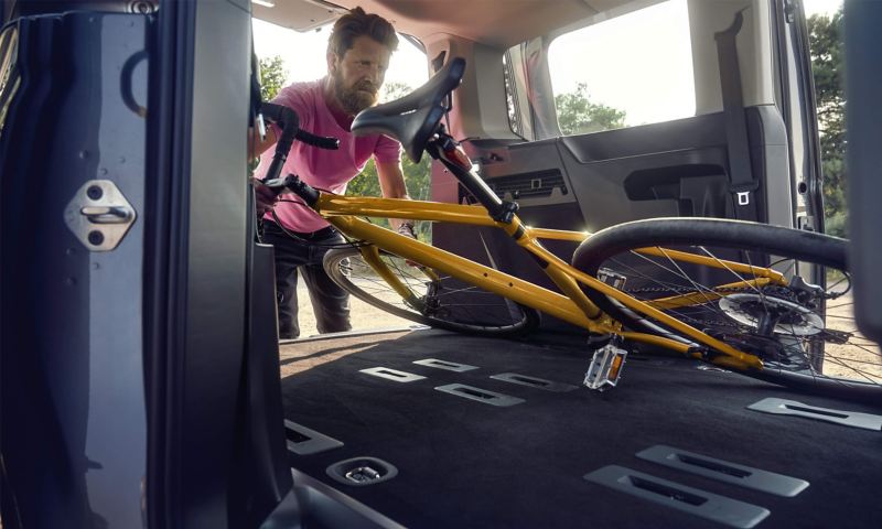 En man lastar in en cykel genom sidodörren på en VW Caddy familjebil