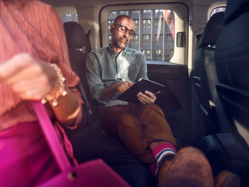 En man sitter inuti en VW Caddy familjebil med en läsplatta i händerna
