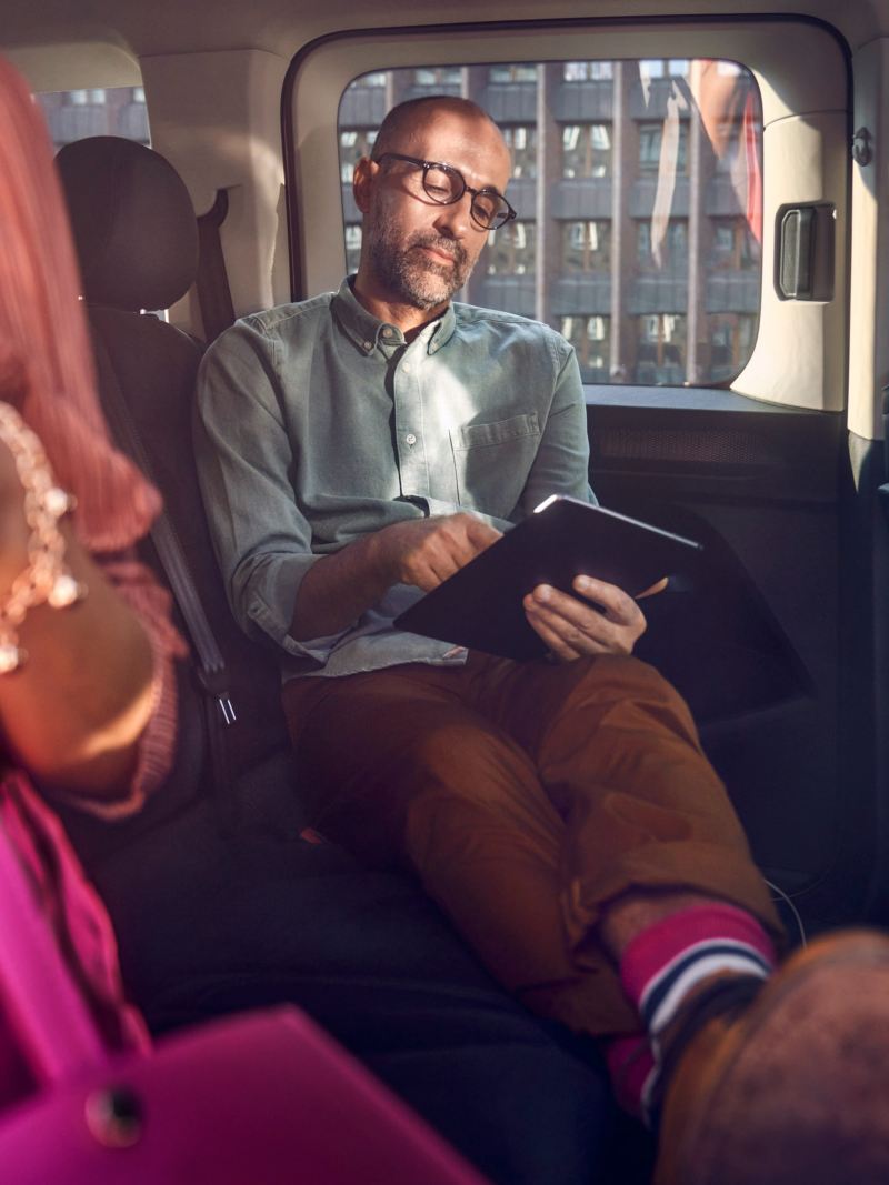 En man sitter inuti en VW Caddy familjebil med en läsplatta i händerna
