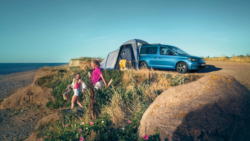 Una familia paseando al lado de un VW Caddy California.