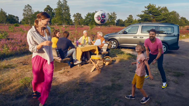 Ein grauer VW Caddy in der Heide mit Familie beim Picknick und Fußball spielen