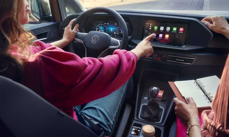 zwei Frauen sitzen in einem VW Caddy und eine Frau bedient das Infotainment-Display.