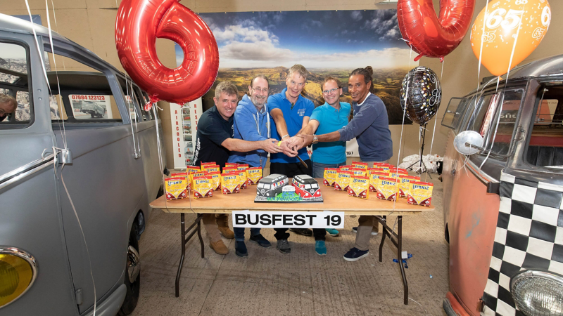 Photo showing a group of people behind a table with party treats on it and baloons around it. 