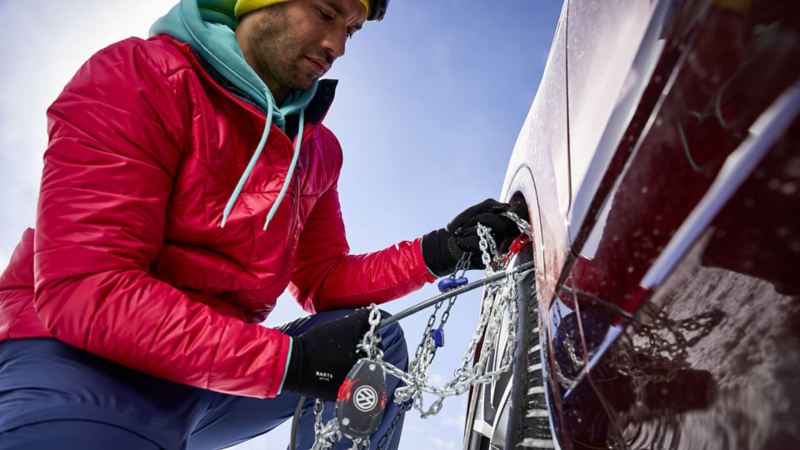 Un homme installe des chaines à neige sur la roue de sa Volkswagen.