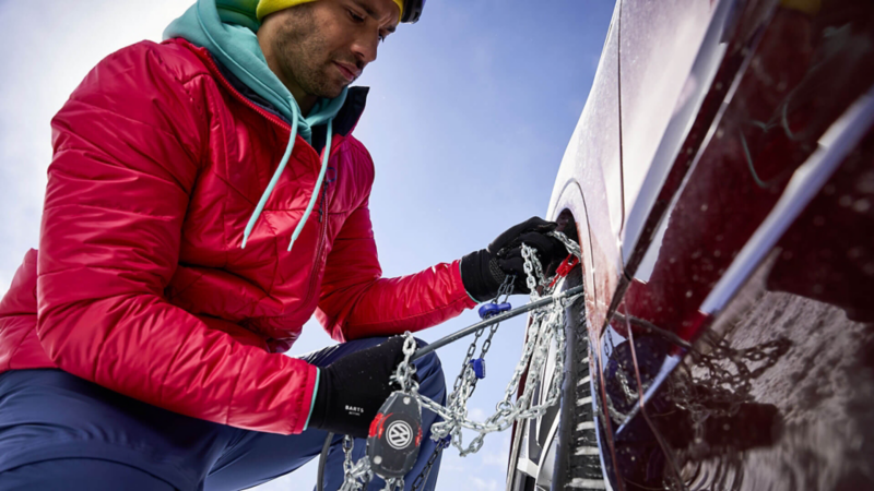 Un homme installe des chaines à neige sur la roue de sa Volkswagen.