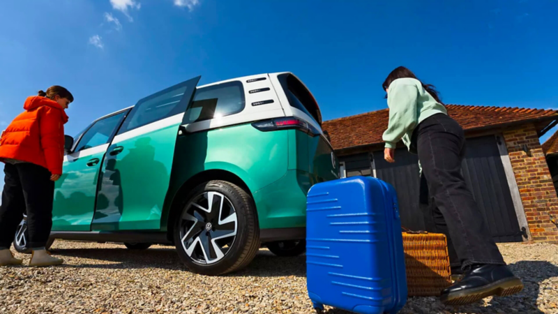 Deux femmes chargent des bagages dans un Volkswagen ID. Buzz vert avec la porte coulissante côté conducteur ouverte.