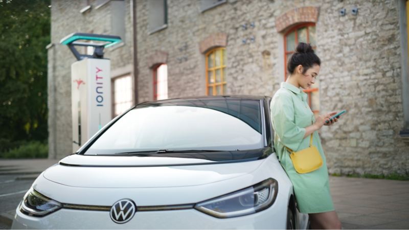 A woman leans against the VW ID.3 while the vehicle is charging at an IONITY charging station.