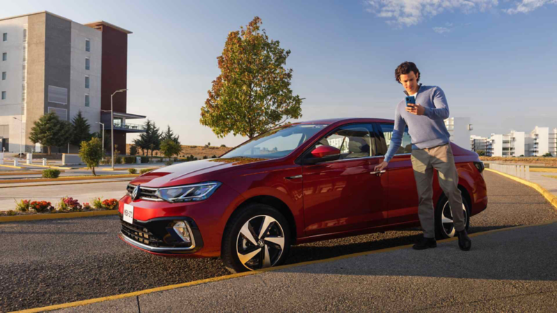 Conductor de Volkswagen abre la puerta mientras ve la aplicación VW en su celular. 