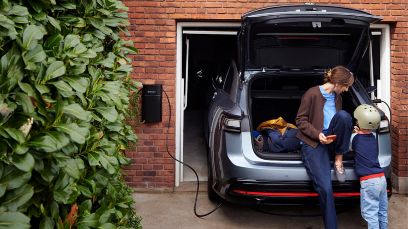 En ID.7 holder i carport og lader. En kvinde sidder i det åbne bagagerum og en dreng er foran hende