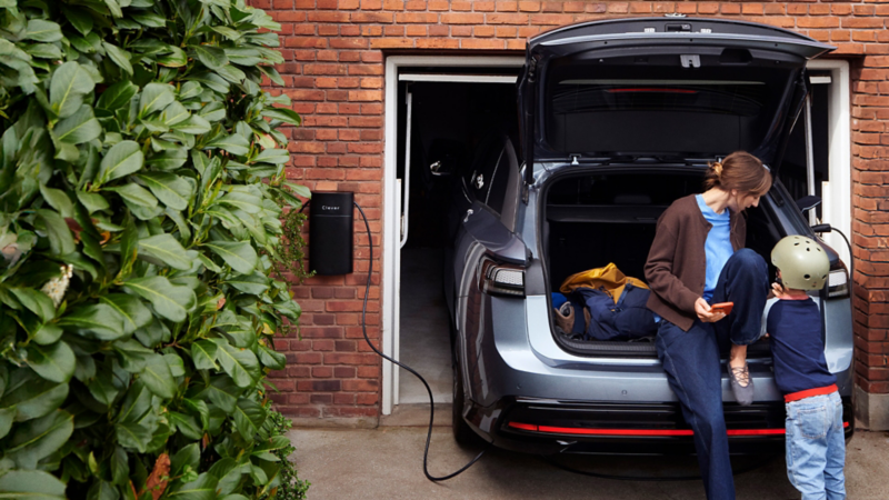En kvinde sidder i bagagerummet i en ID.7 der lader i en carport.