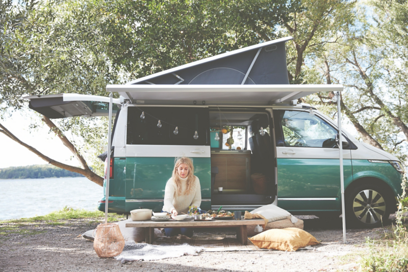 Kvinna sitter vid ett bord utanför en Volkswagen campervan med öppen baklucka.