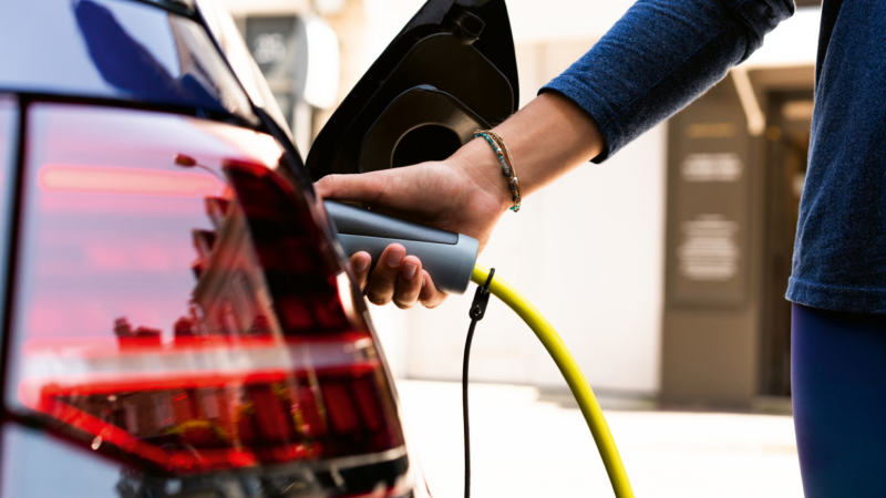 Detalle de una mano conectando un cargador eléctrico a un Volkswagen