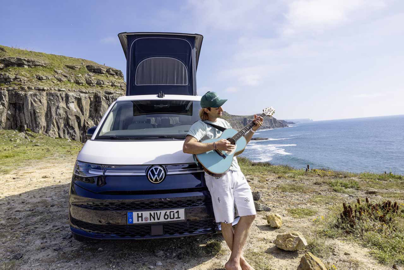 Una persona apoyada en una Nueva California tocando la guitarra en una costa natural al Sol