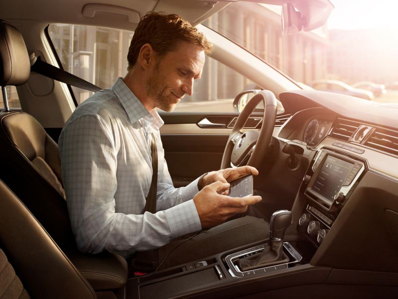 Hombre sentado en el puesto de conducción de un Volkswagen comercial usando un móvil con MirrorLink