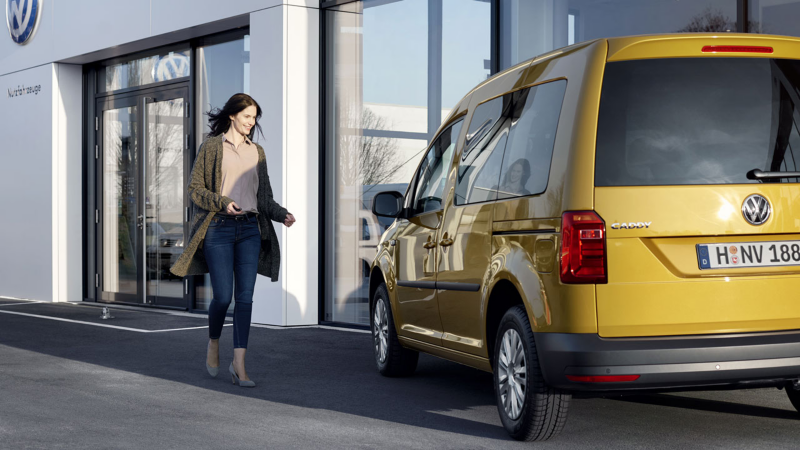 Una mujer caminando hacia un VW Caddy estacionado.