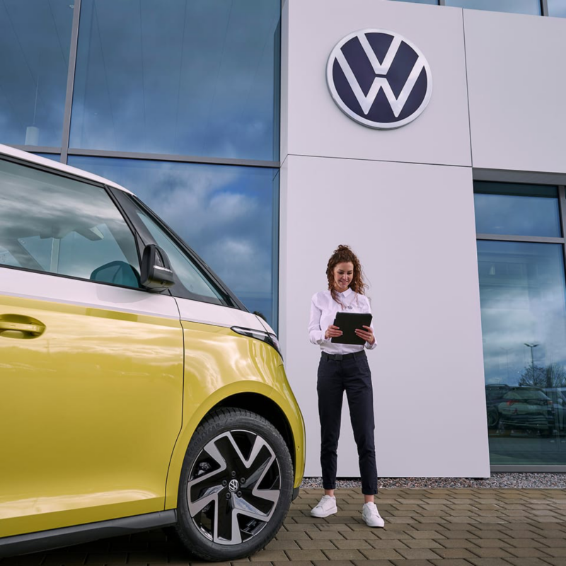 Una agente de servicio en un concesionario VW junto a una ID. Buzz