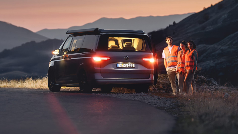 Tres personas con chalecos reflectantes junto a una furgo Volkswagen en la carretera
