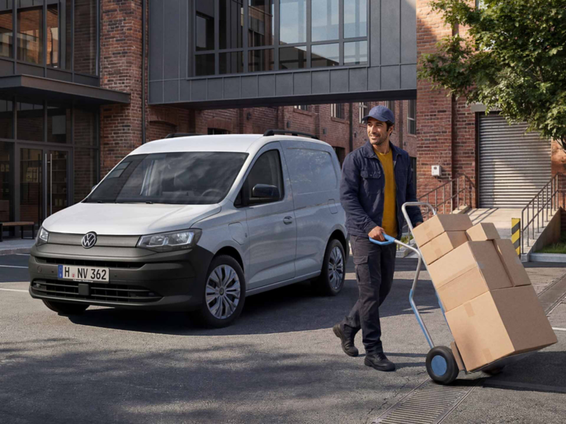 Un Caddy Cargo de ocasión aparcado en un exterior de trabajo y una persona transportando cajas