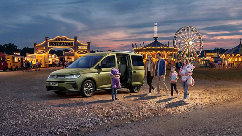 El Nuevo Caddy de Volkswagen aparcado delante de una feria y personas disponiéndose a entrar en ella