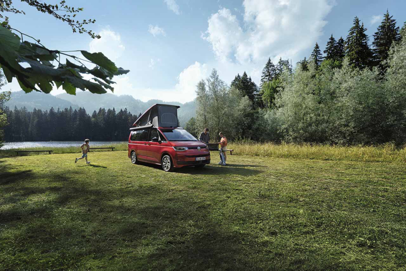 Un Nuevo California aparcado en el bosque con el techo elevable delante de un lago