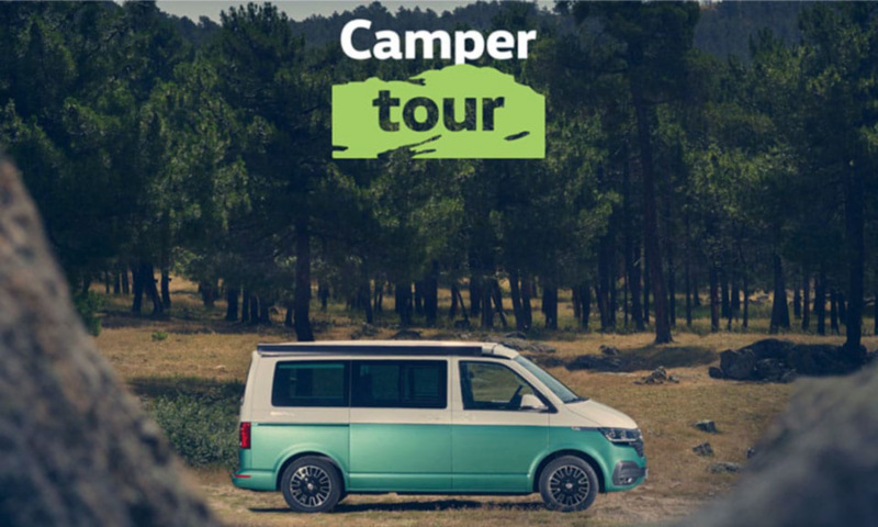 Una Camper de Volkswagen aparcada entre la naturaleza con un cartel de Camper tour