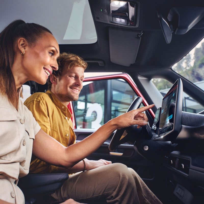 Una pareja en el interior de un Volkswagen señalando la pantalla frontal