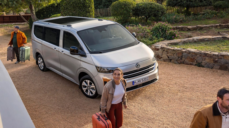 Un Volkswagen Caravelle aparcado y personas llevando maletas