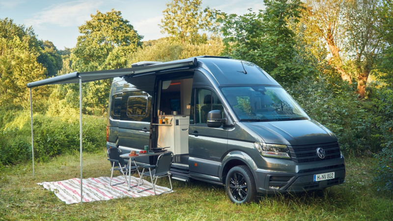 Una Volkswagen Grand California con la puerta lateral abierta y el toldo desplegado en el campo