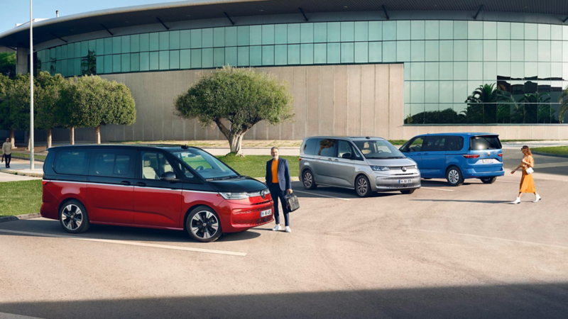 Personas junto a furgonetas de Volkswagen en un parking frente a un edificio moderno