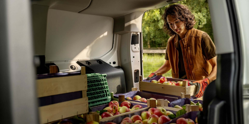 Una persona cargando cajones de fruta en el maletero de un VW Caddy