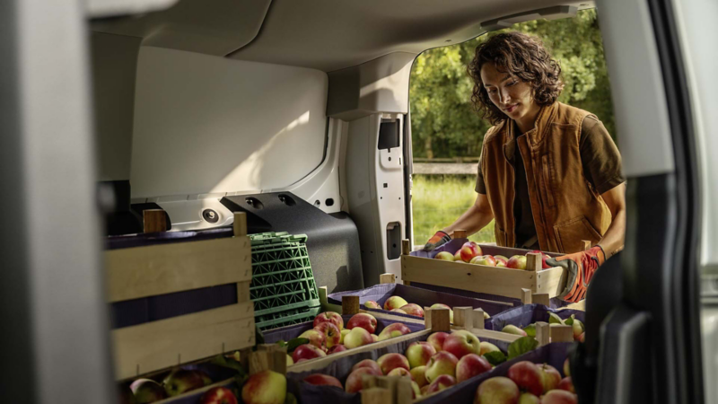 Una persona cargando cajones de fruta en el maletero de un VW Caddy