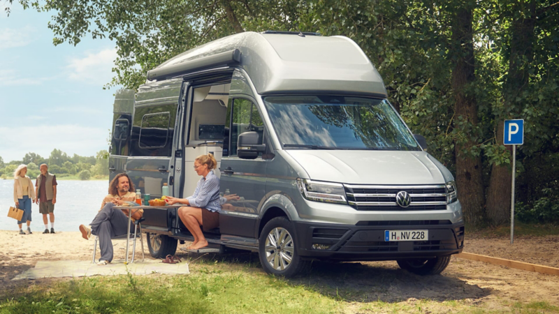 Un grupo de personas junto a una VW Grand California estacionada en un prado verde.