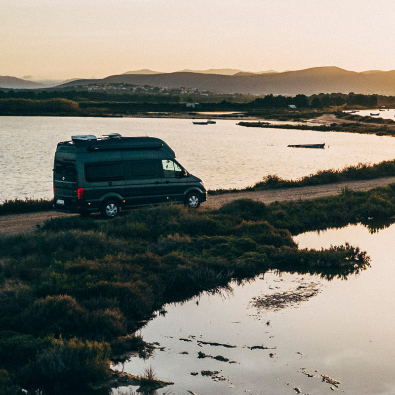 VW Grand California en una carretera junto a un lago al atardecer