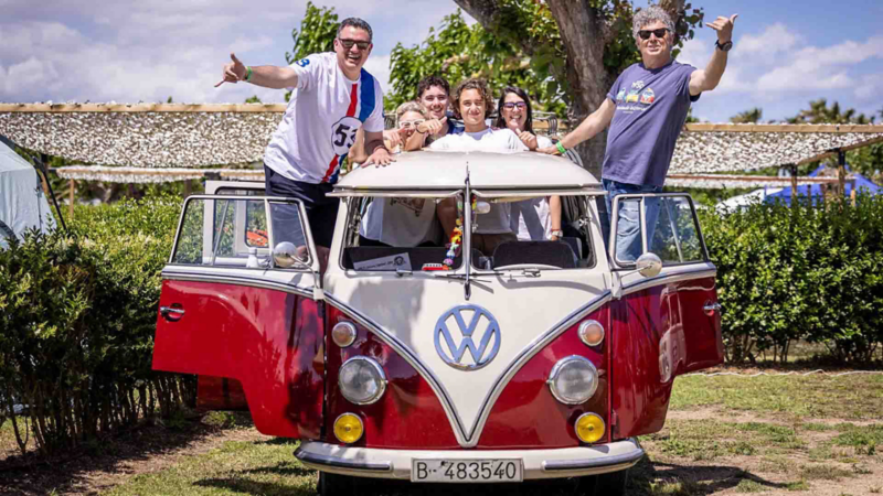 Una furgo clásica de Volkswagen roja y blanca aparcada en un ambiente al aire libre con personas encima de ella