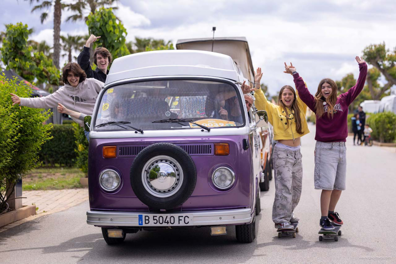 Una furgo clásica de Volkswagen morada y blanca con personas alrededor felices