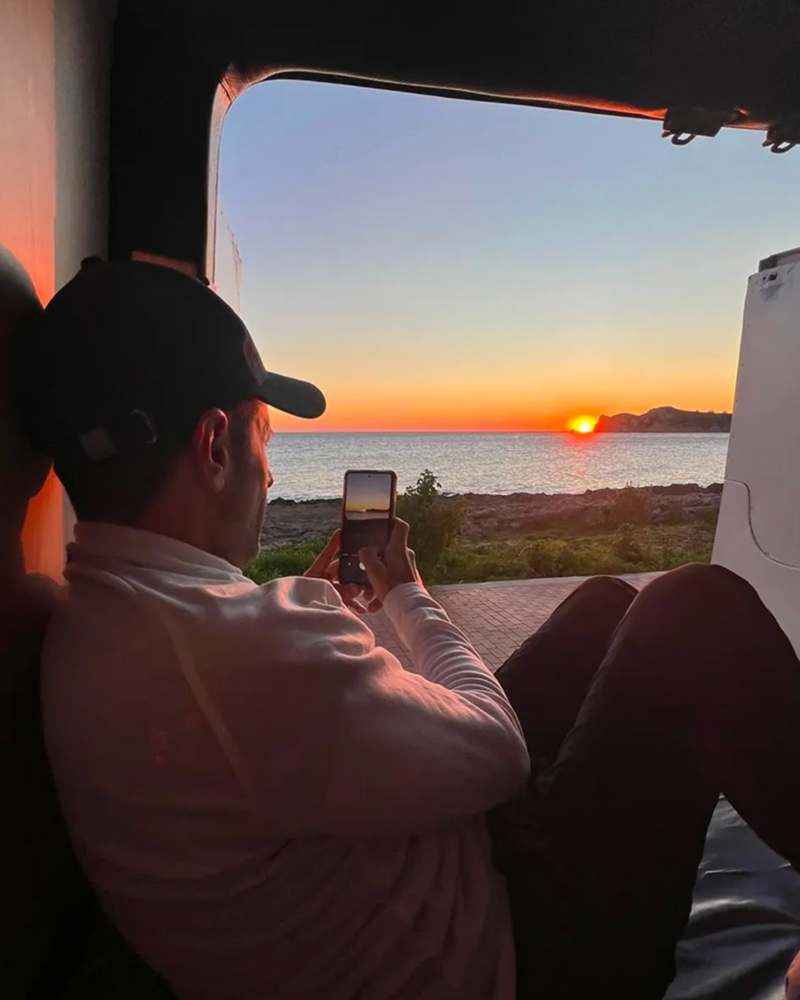 Una persona sentada en su furgo Volkswagen mientras fotografía el atardecer en un espacio natural