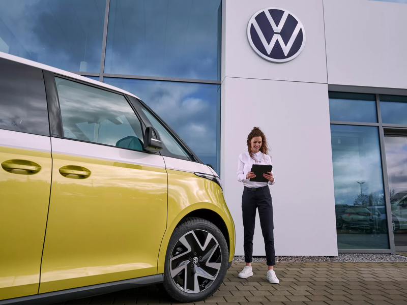 Una agente de servicio Volkswagen junto a un Volkswagen ID. Buzz bicolor