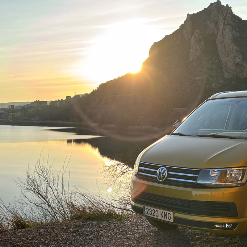 Una furgo Volkswagen con un paisaje de lago y montaña al atarceder