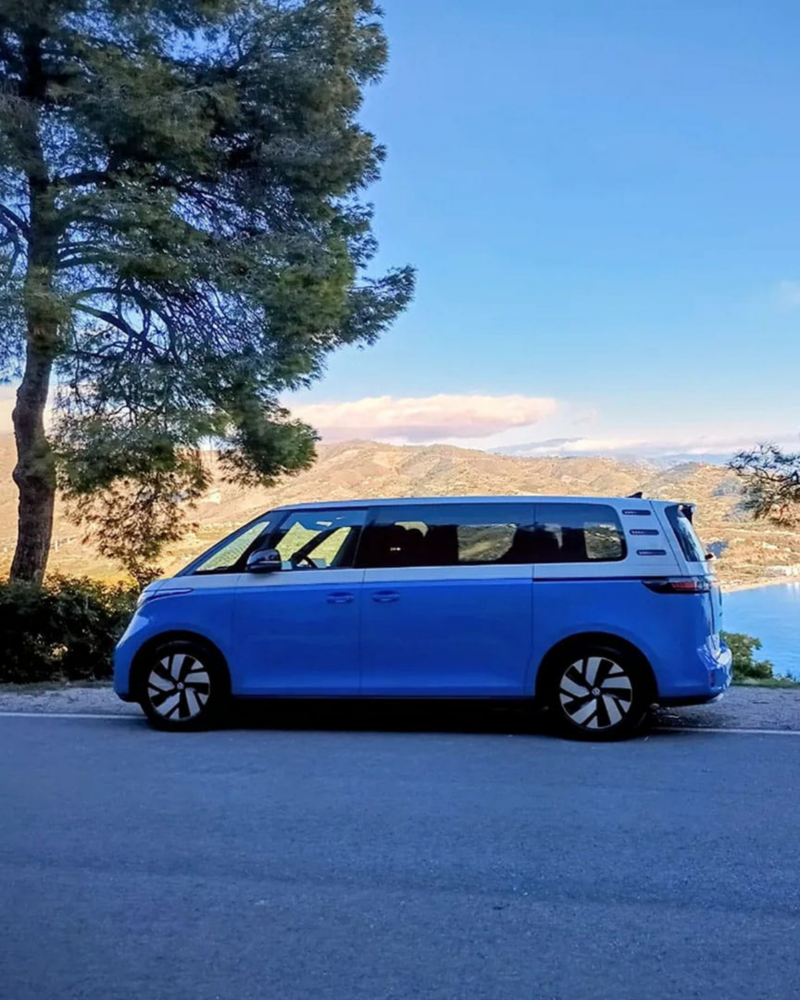 Una ID.Buzz aparcada a un costado de una carretera con la playa y montaña de fondo