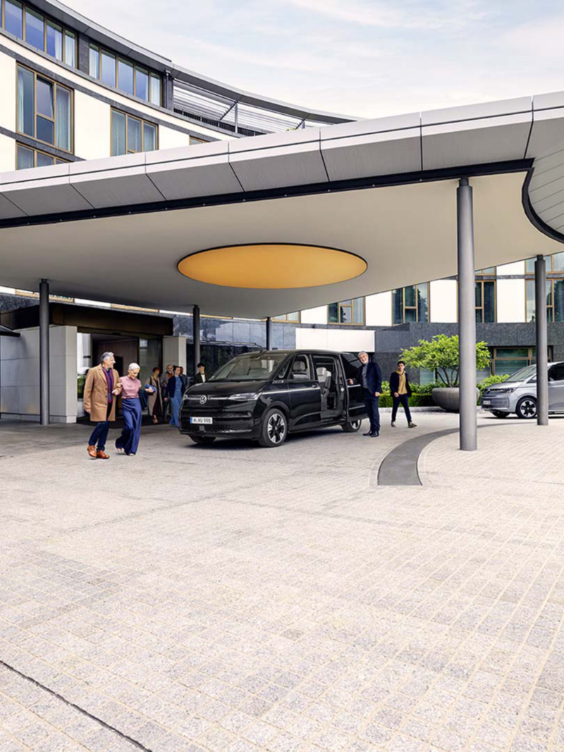 Una Multivan 6.1 de Volkswagen aparcada delante de un edificio moderno con personas alrededor