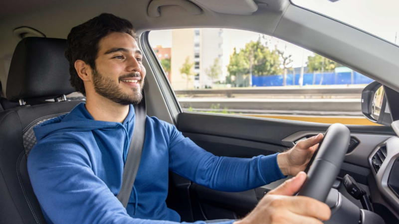 Hombre joven conduce auto Volkswagen por la ciudad mientras sonríe.