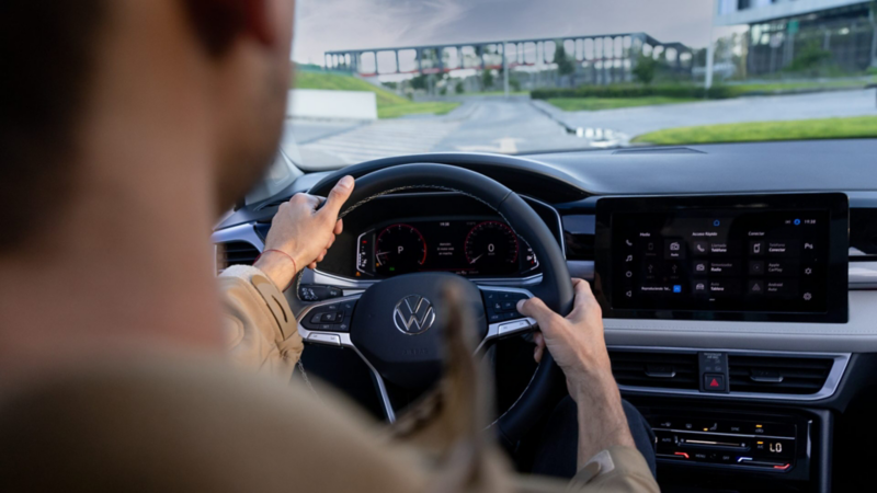 Conductor maneja un auto Volkswagen con volante multifunciones y pantalla digital de infoentretenimiento.