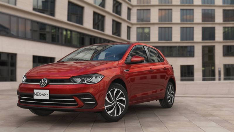 Volkswagen Polo de color rojo estacionado cerca de un edificio con decenas de ventanas. 