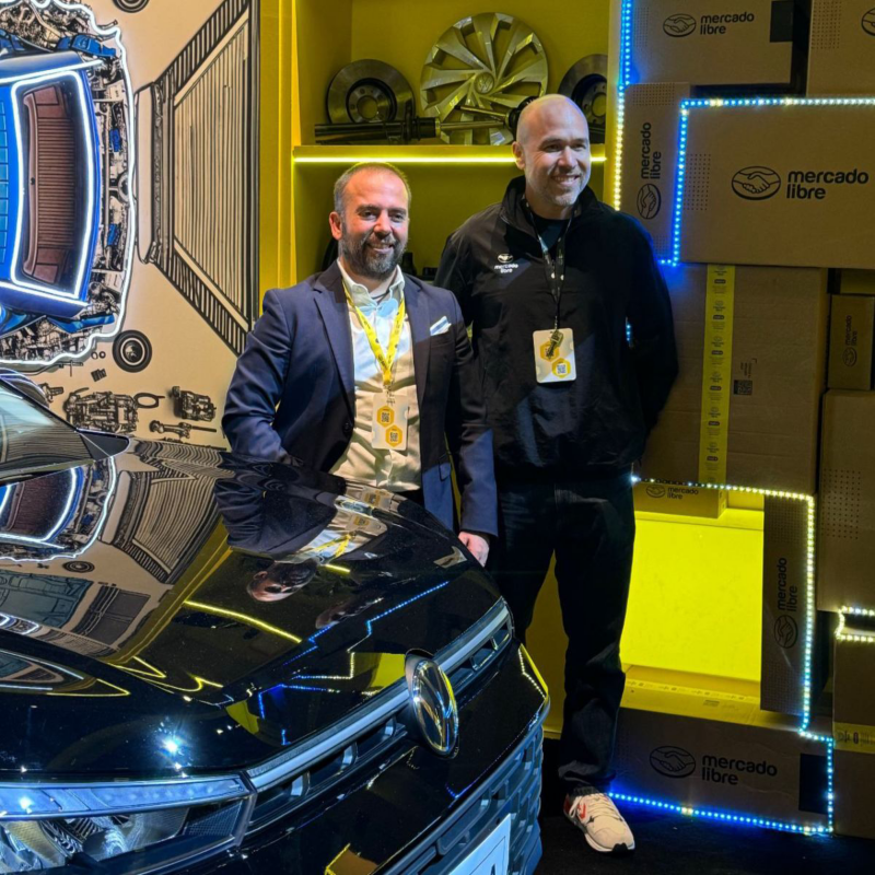 Directivos de Volkswagen posan en stand de Mercado Libre a lado de vehículo VW.