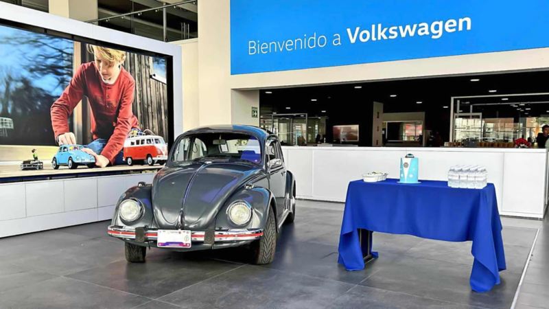 Interior de concesionaria Volkswagen con Vocho gris en el Vocho Fest 2024. 