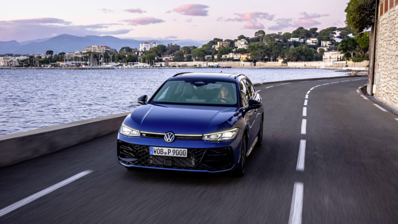 Une VW Passat R-Line bleue roule sur une route au bord de la mer.